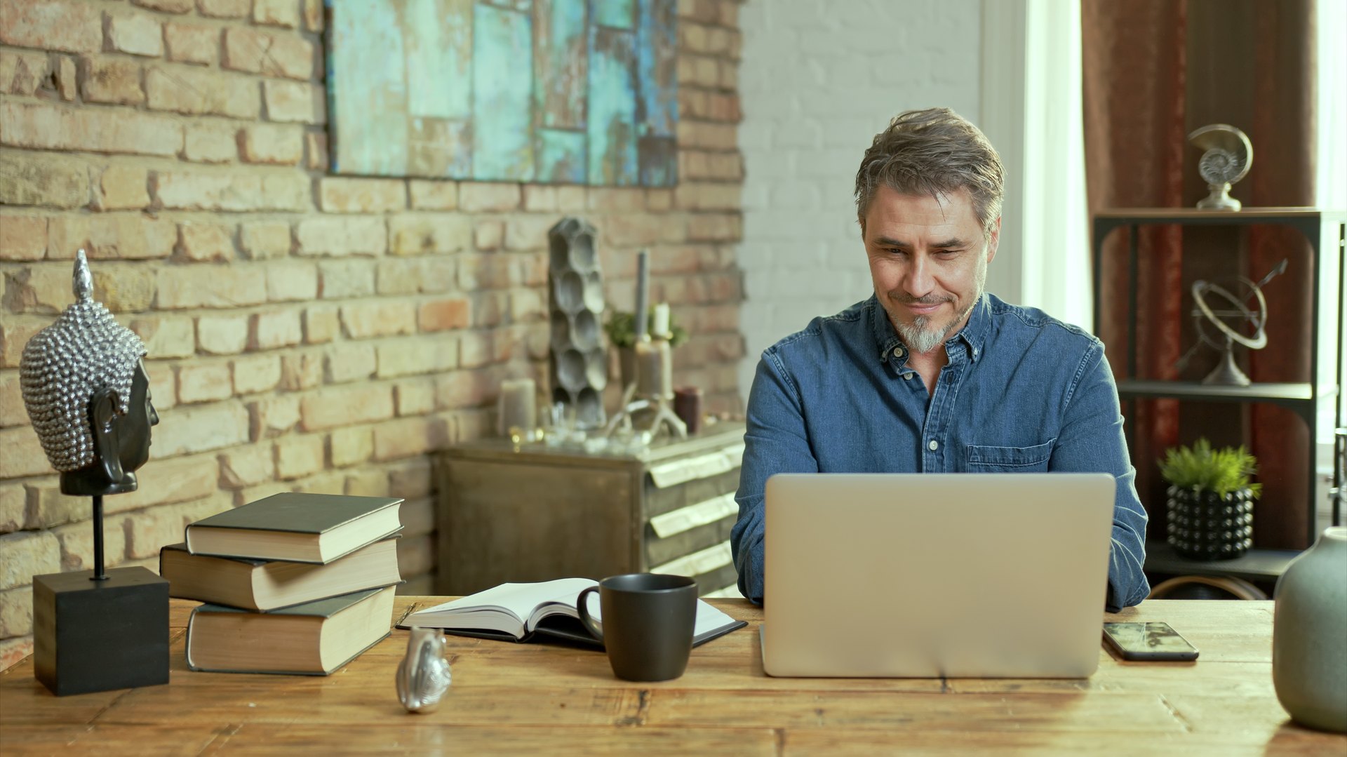 Person working with a laptop and open book at a wooden desk