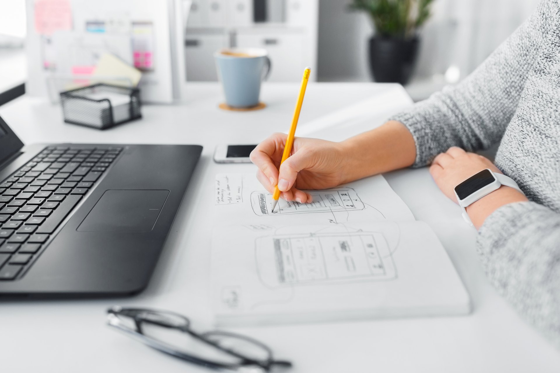 Person drawing interface plans beside a laptop