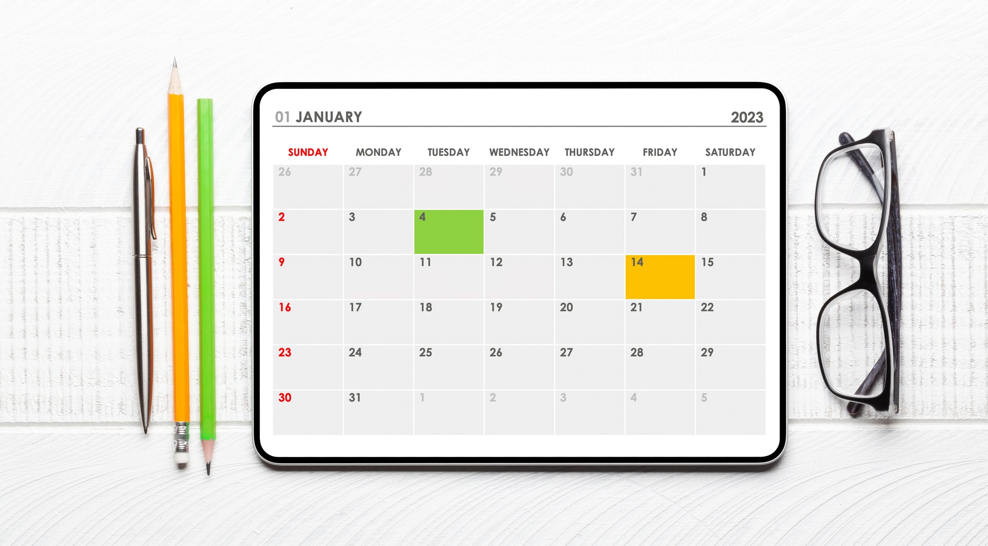 Calendar displayed on a tablet beside pencils and glasses